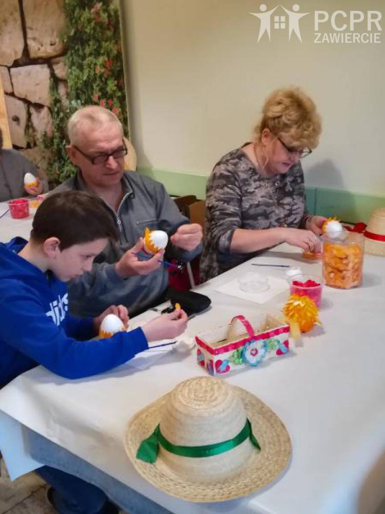 Zdjęcie: Chłopiec i dwie dorosłe osoby siedząc przy stole przyczepiają drobne elementy do modelu